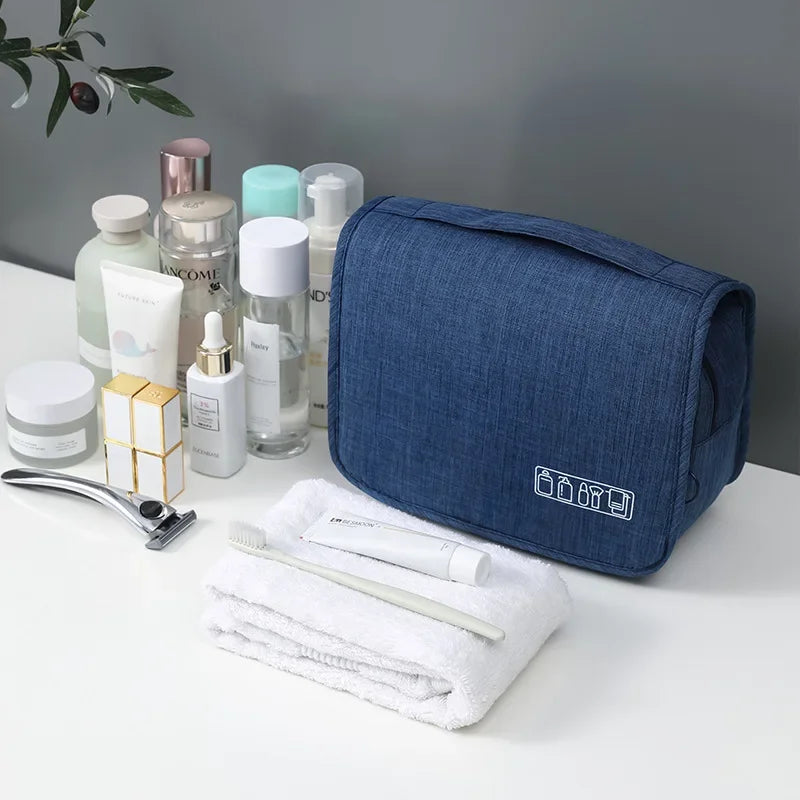 Un sac organisateur en tissu bleu marine avec divers produits de soin et de beauté, arrangés autour, sur une surface blanche.