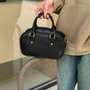 A hand holds a black vintage PU leather shoulder bag against a light-colored background.