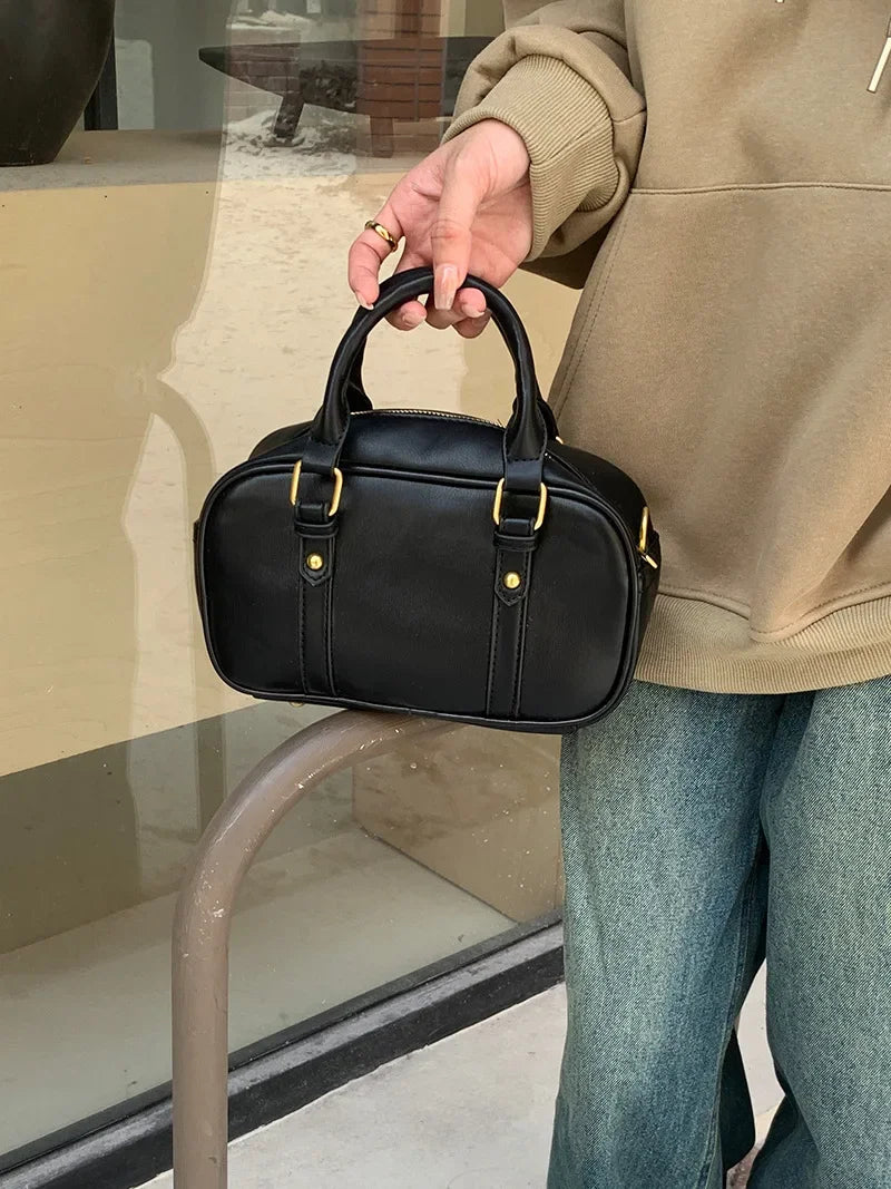 A hand holds a black vintage PU leather shoulder bag against a light-colored background.