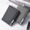 A dark gray slim vertical men's card wallet resting on a white surface next to a magazine.