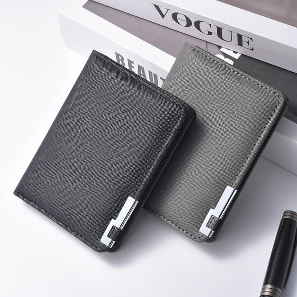 A dark gray slim vertical men's card wallet resting on a white surface next to a magazine.