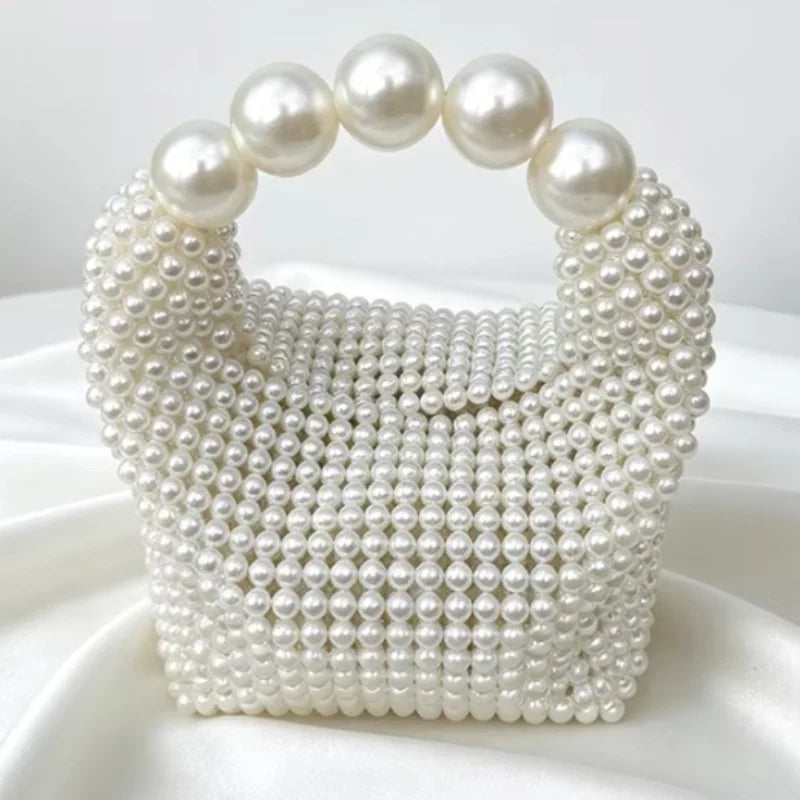 A white pearl beaded clutch bag with a textured surface displayed on a white fabric.