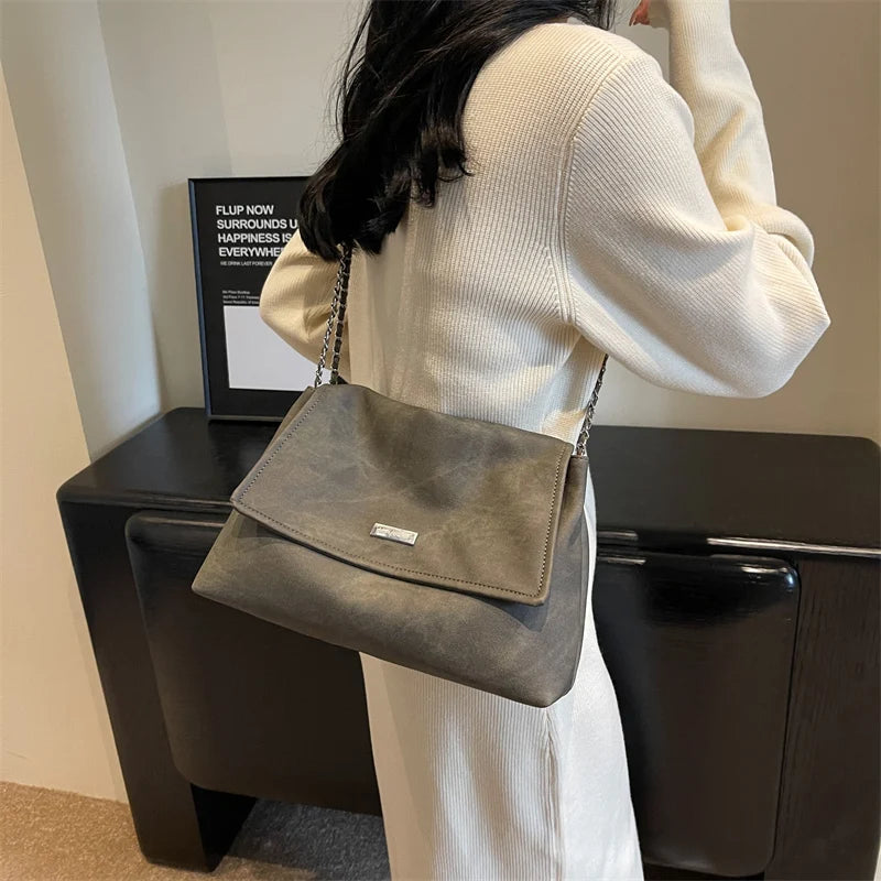 Una mujer sostiene un bolso de cuero gris contra un suéter de punto blanco en un entorno moderno.