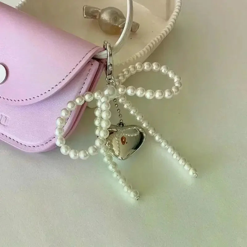 A pearl bowknot keychain with a heart charm is displayed next to a pink leather pouch.
