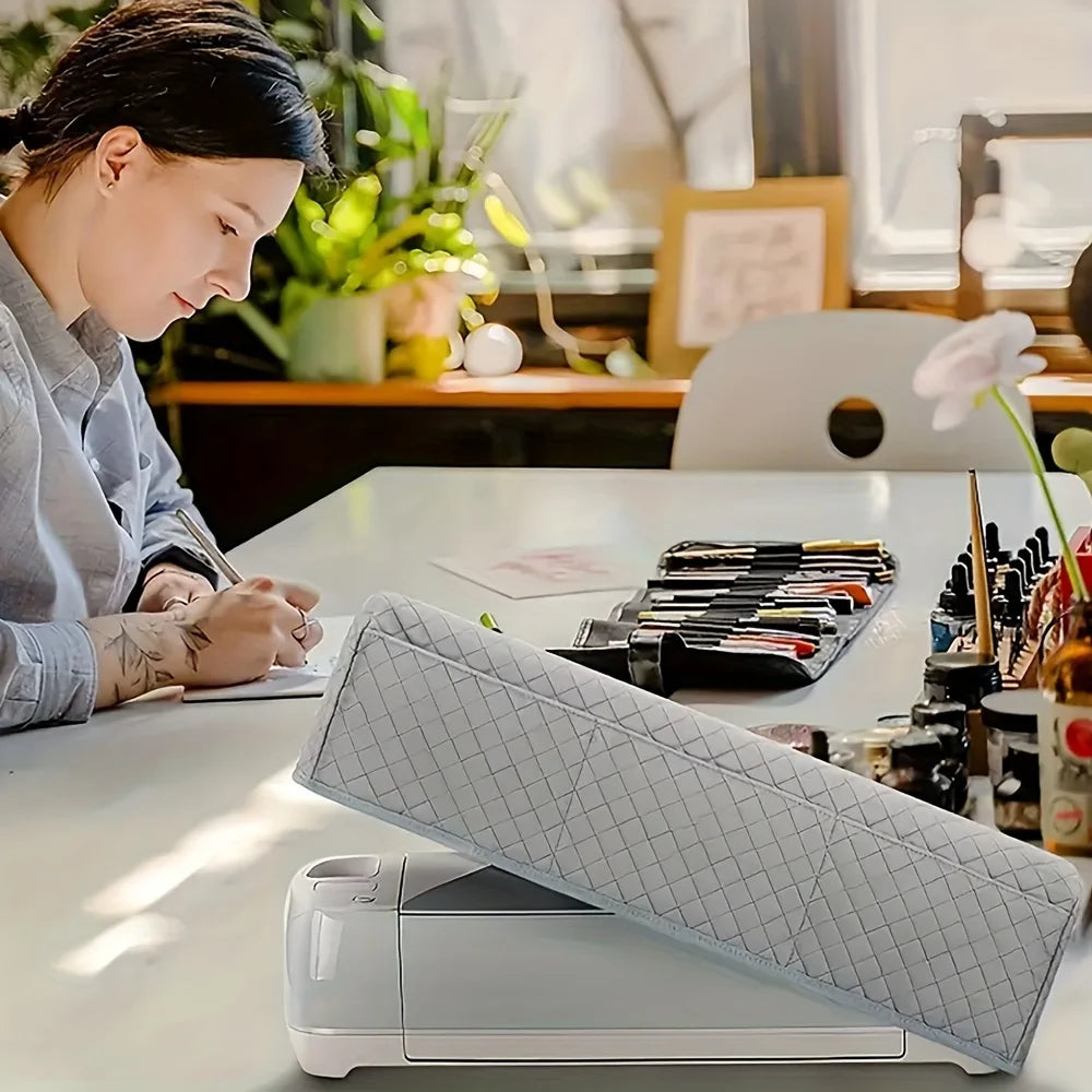A light gray protective cover for a Cricut Maker device resting on a white table.