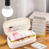 A pink pencil case with a clear lid is shown open, containing various pens and pencils on a wooden surface.