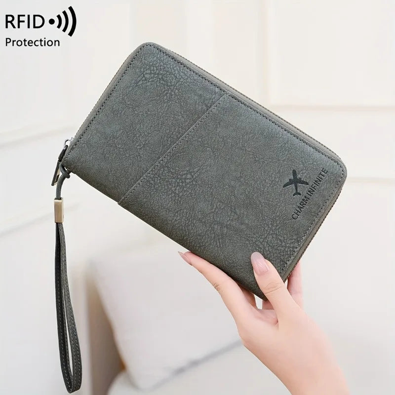 A dark gray leather passport wallet with a wrist strap is being held by a hand.