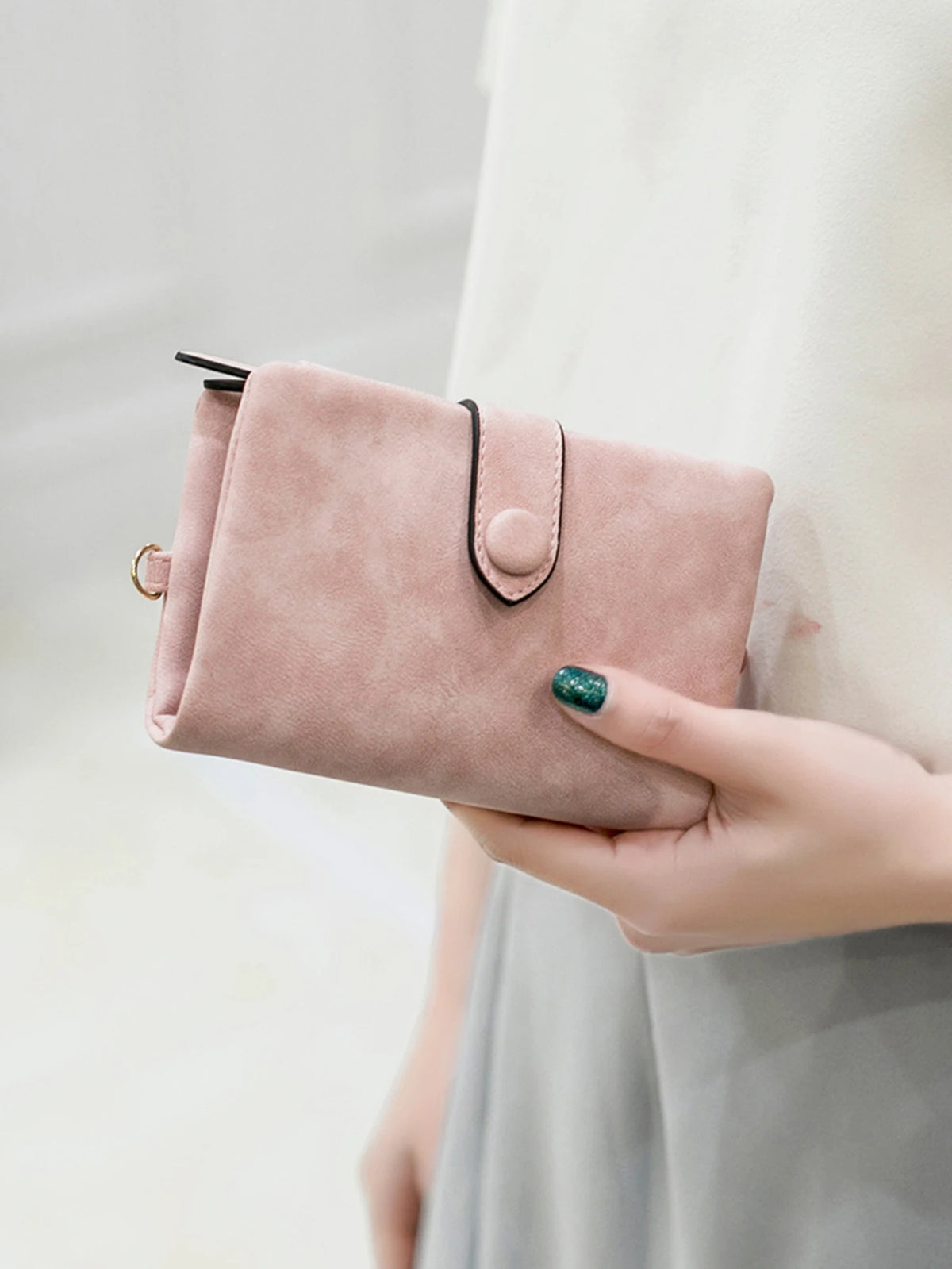 A light pink multi-slot frosted card wallet held by a person, featuring a black pull tab and an emerald green ring finger nai