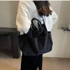 A person is holding a black corduroy multi-pocket tote bag over their shoulder in a light-colored jacket.