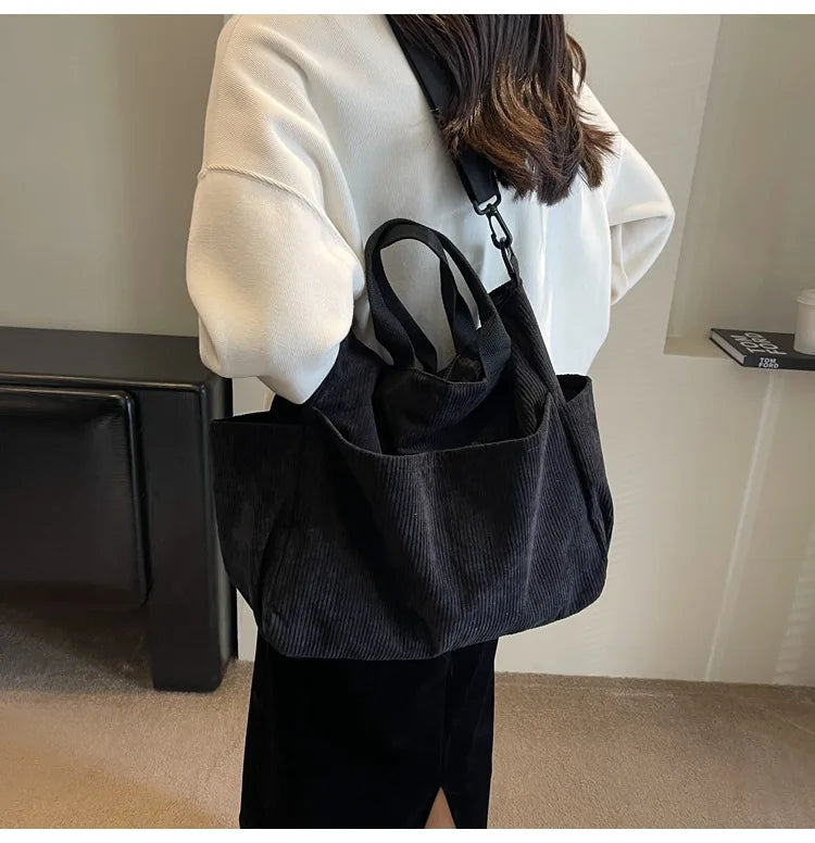 A person is holding a black corduroy multi-pocket tote bag over their shoulder in a light-colored jacket.