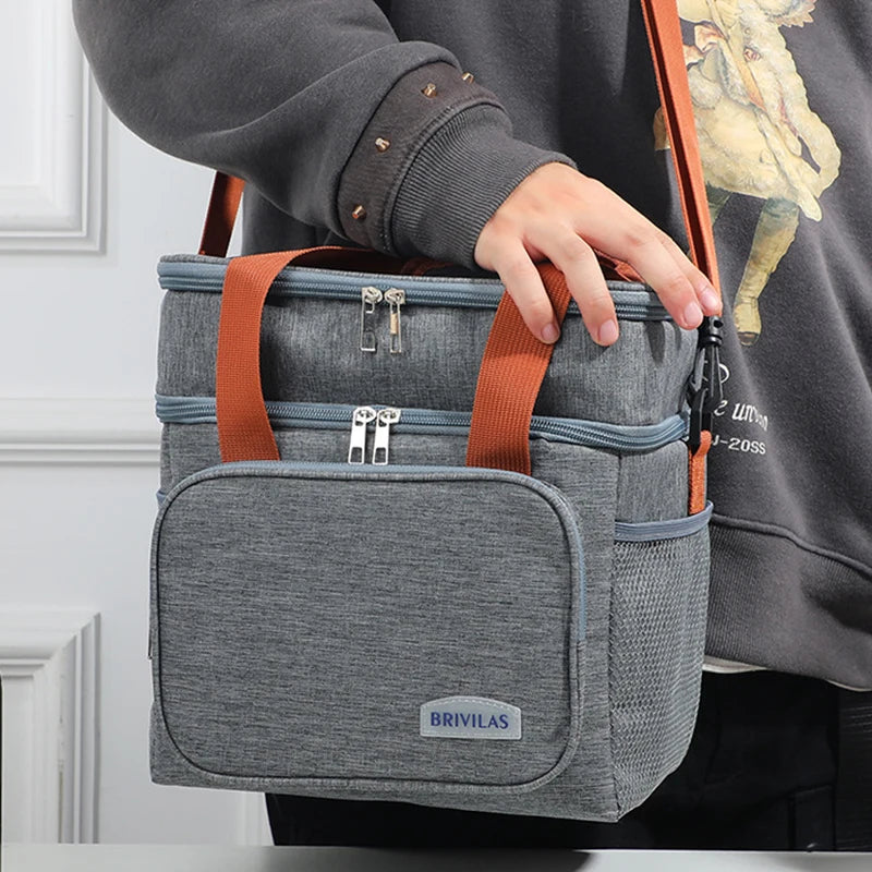 Una persona sostiene una bolsa térmica gris de doble capa con correas naranjas y una manga marrón.