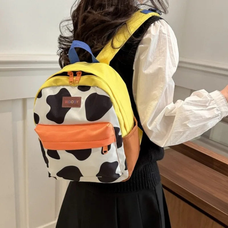 A woman is wearing a yellow backpack with a cow print design and an orange accent on her back.