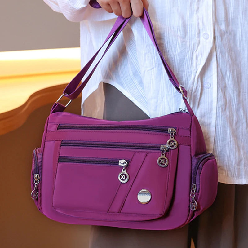 A magenta waterproof nylon crossbody tote bag with silver hardware being held by a person wearing a white shirt.