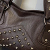 A close-up of a dark brown leather tote bag featuring decorative metal rivets on the front panel.