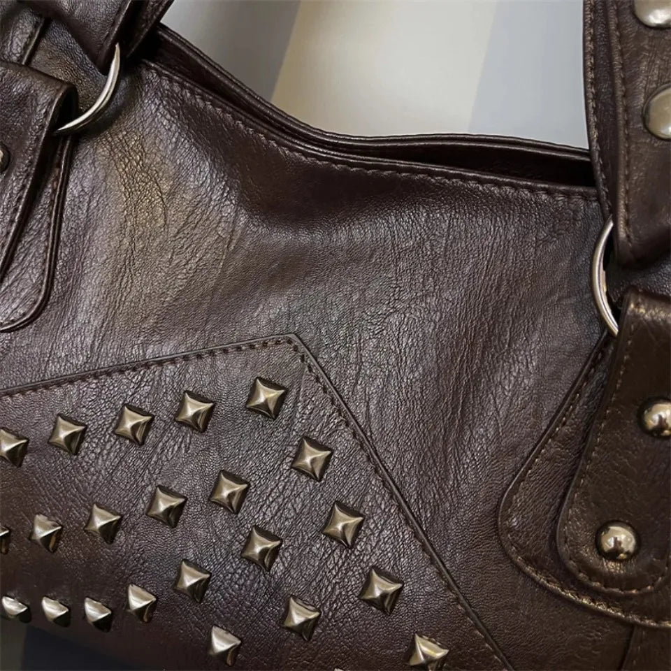 A close-up of a dark brown leather tote bag featuring decorative metal rivets on the front panel.