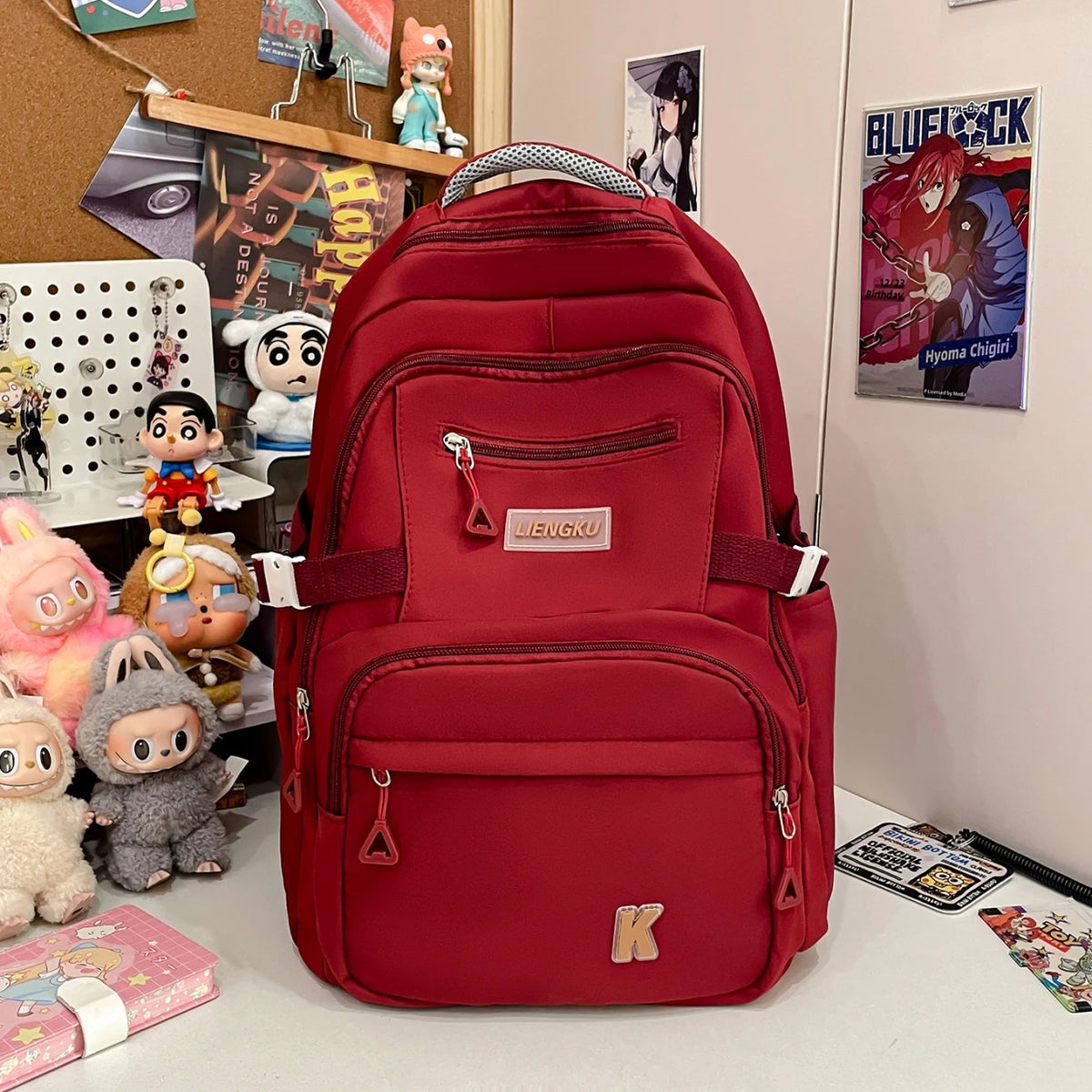 A red backpack with a gray strap and pockets is displayed on a white surface next to various collectibles.