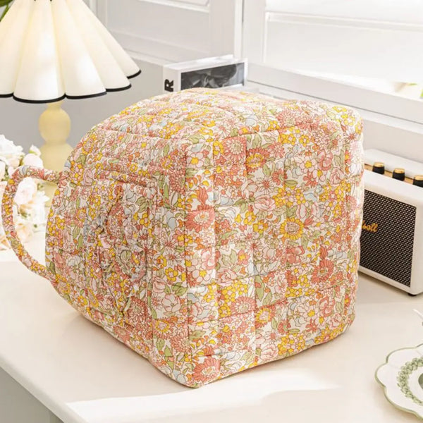 A quilted fabric storage basket with floral pattern and carry handles sitting on a white surface.