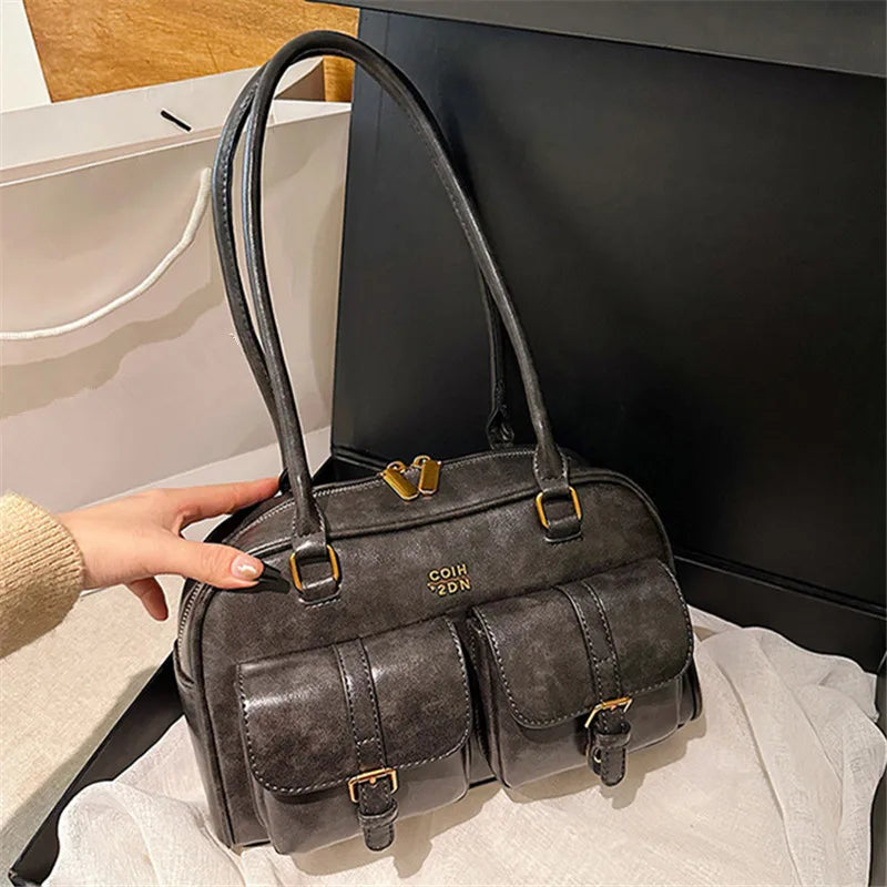 A dark gray leather crossbody bag with gold hardware resting on a light surface.