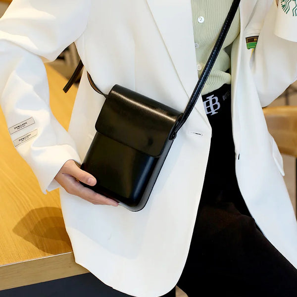 A person holds a black vintage PU leather crossbody bag with an adjustable strap under a white blazer.