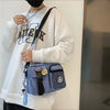 A woman wearing a white sweatshirt and black clothing holds a light blue canvas shoulder bag with a strap.