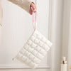 A white quilted puffer makeup bag with pink strap is being held by a hand.