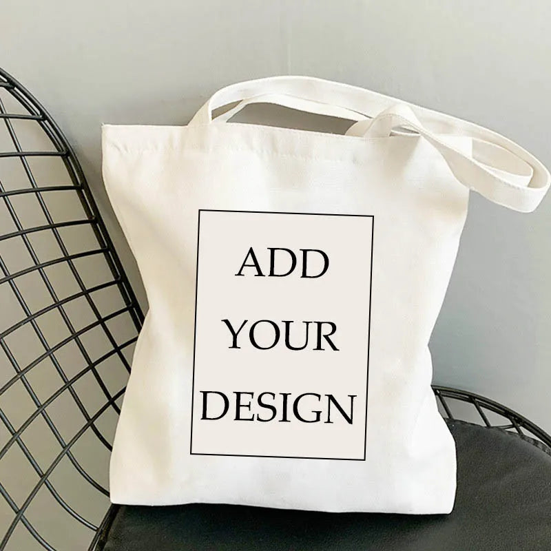 Sac de courses en toile blanche avec une boîte rectangulaire noire à l'avant indiquant 'Add Your Design'.