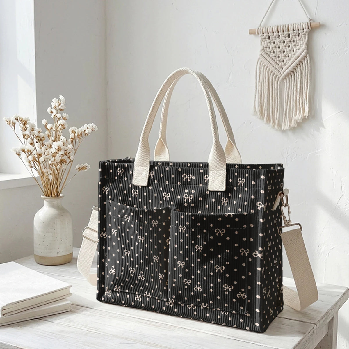 Sac fourre-tout en velours côtelé noir à pois blancs et poignées beige clair, exposé sur une surface en bois blanc.