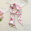 Foulard de cheveux floral soie rose et blanc drapé sur une surface blanche à côté d'une carte de remerciement.