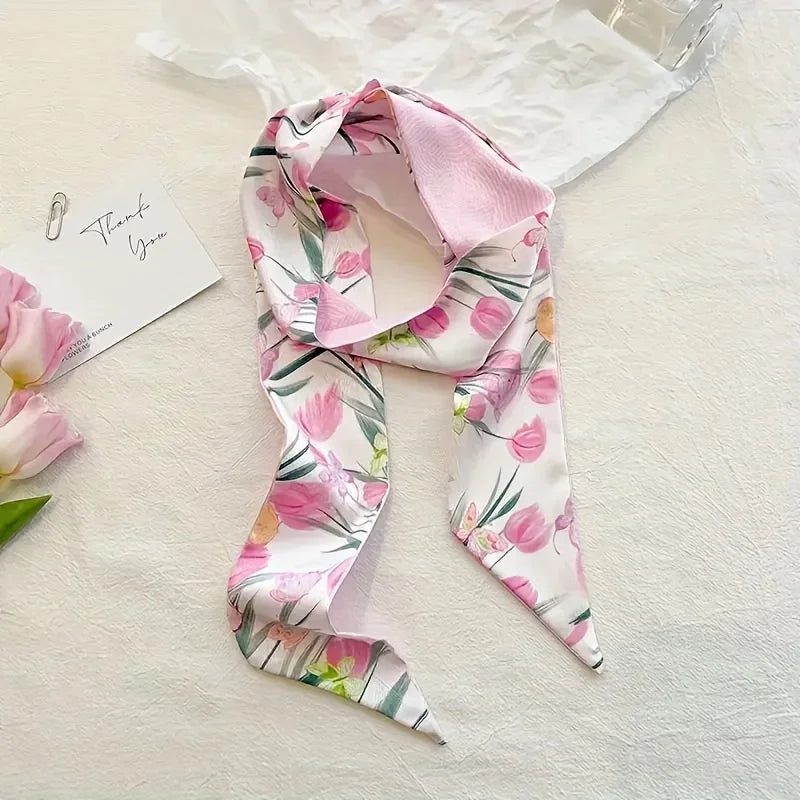 Foulard de cheveux floral soie rose et blanc drapé sur une surface blanche à côté d'une carte de remerciement.