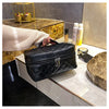 A hand holds a black PU embroidery makeup storage pouch on a marble surface next to skincare products.