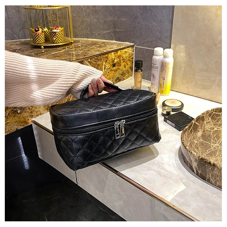 A hand holds a black PU embroidery makeup storage pouch on a marble surface next to skincare products.