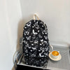 A black backpack featuring a white butterfly pattern, resting on a metal shelf next to a cup of coffee.