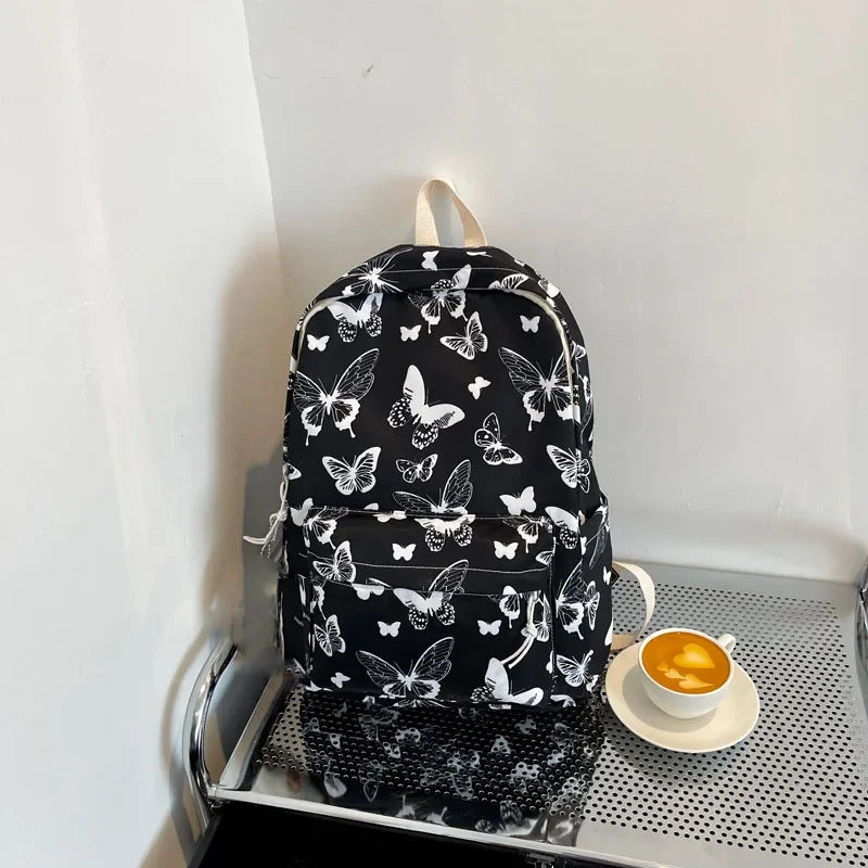 A black backpack featuring a white butterfly pattern, resting on a metal shelf next to a cup of coffee.