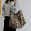 A person wearing a gray sweatshirt and black pants holds a leopard print canvas crossbody tote bag.