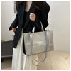A woman holds a silver tote bag with leather straps against a white background.