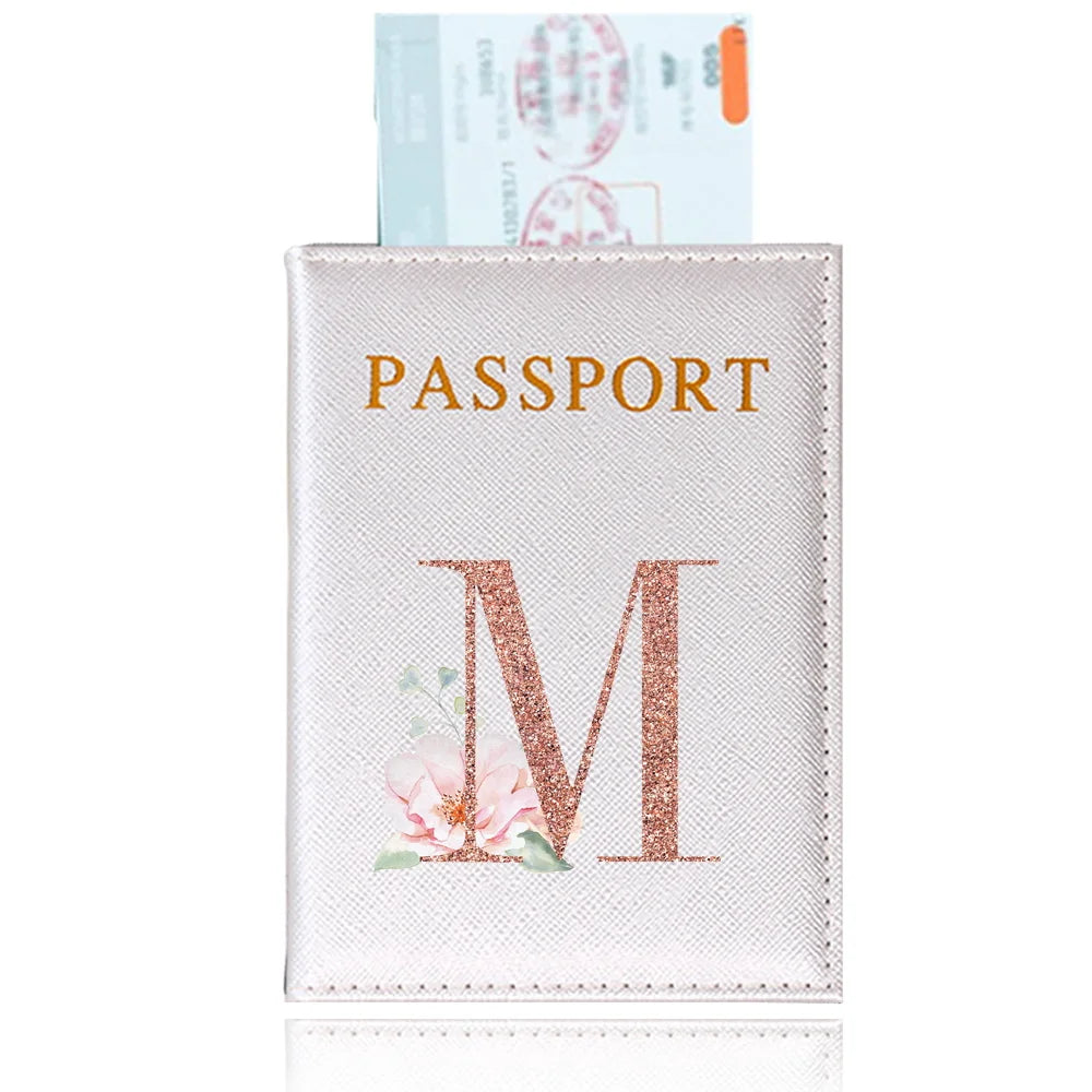 A pink leather passport holder with a gold embossed letter M and a floral design.