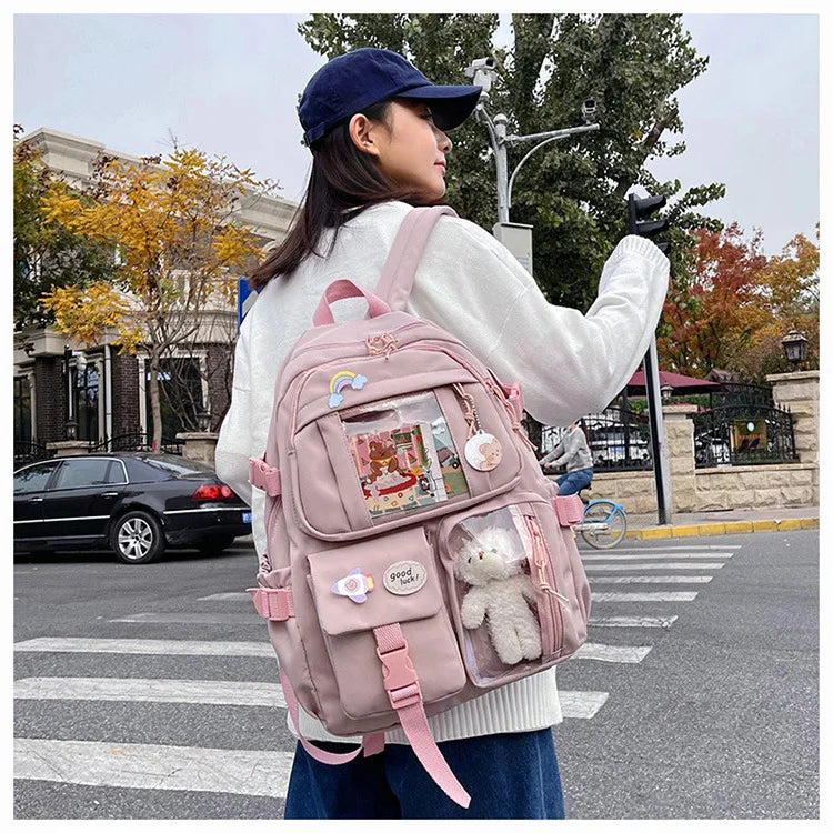 A woman wearing a pink backpack with a padded laptop compartment walks across a crosswalk in an outdoor setting.