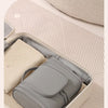 A gray hanging toiletry bag is shown open inside a light-colored box on a patterned surface.