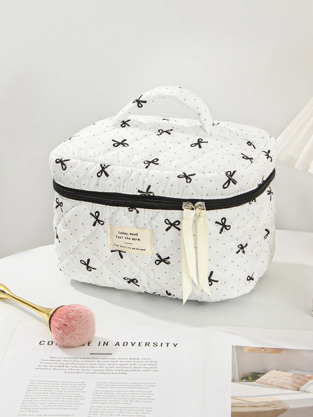 A white quilted makeup bag with black polka dots and a black zipper, featuring a light yellow ribbon.