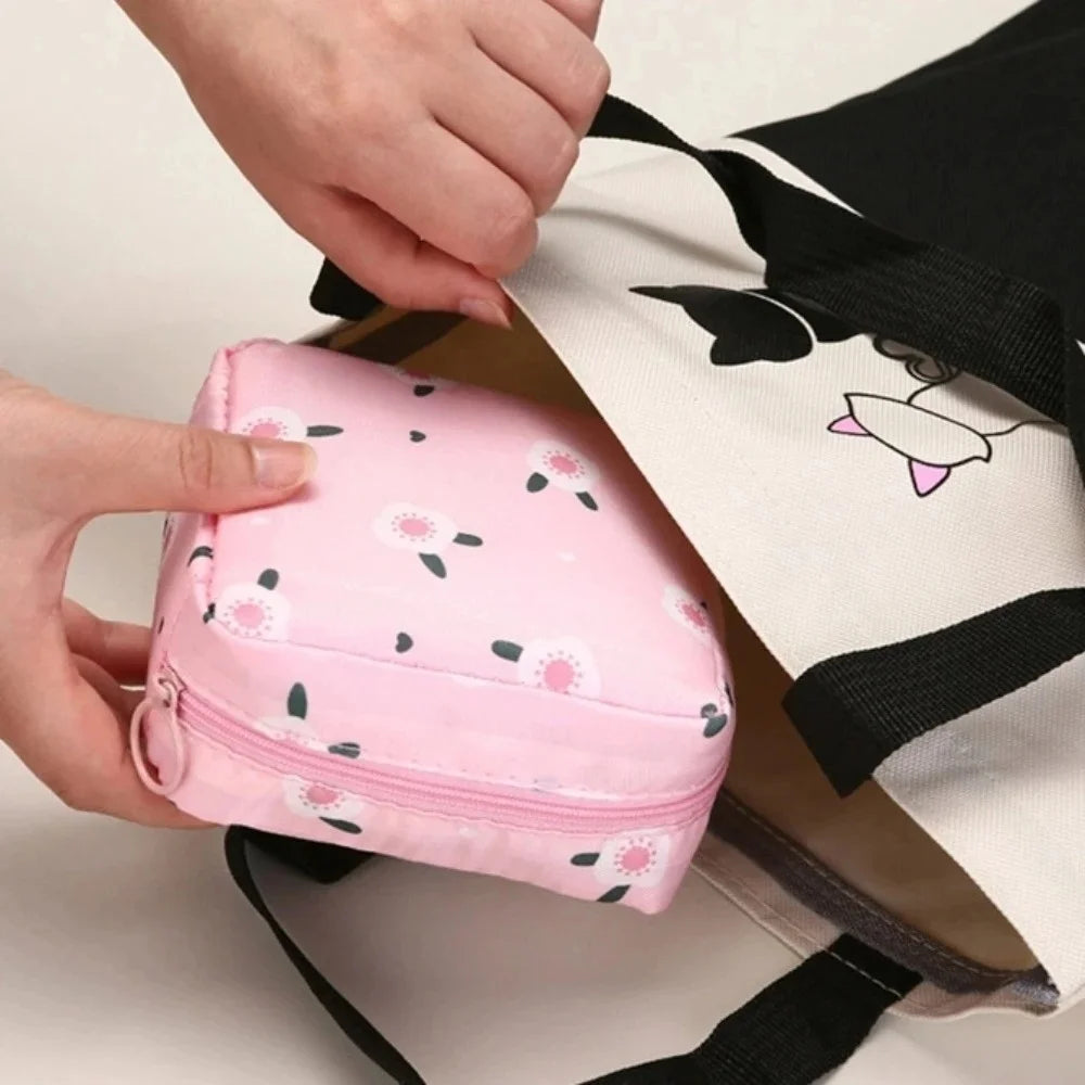 A hand is holding a pink portable waterproof sanitary napkin storage pouch with black straps.