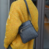 A person wearing a yellow knit sweater is holding a black lightweight crossbody sling bag.