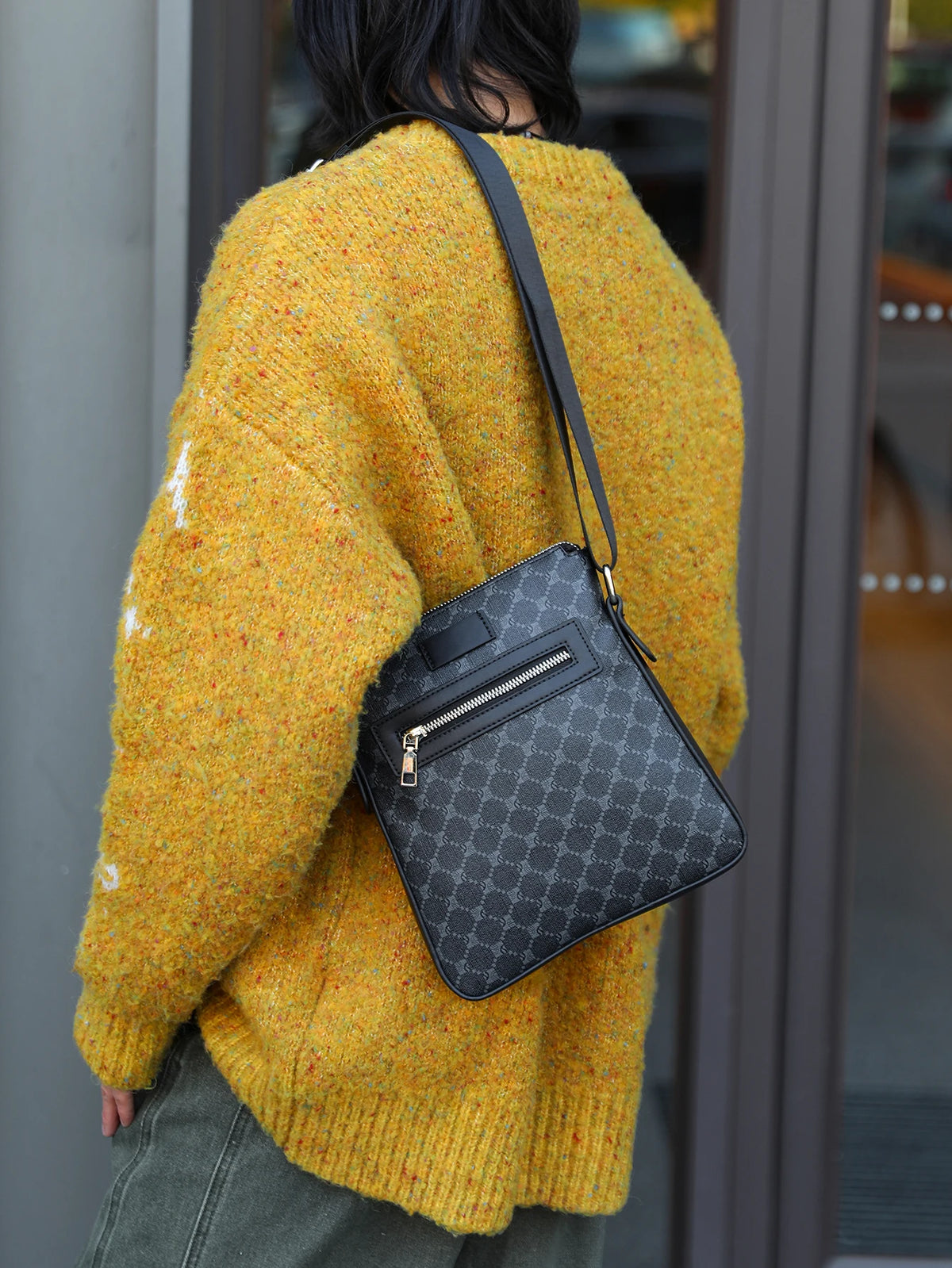 A person wearing a yellow knit sweater is holding a black lightweight crossbody sling bag.