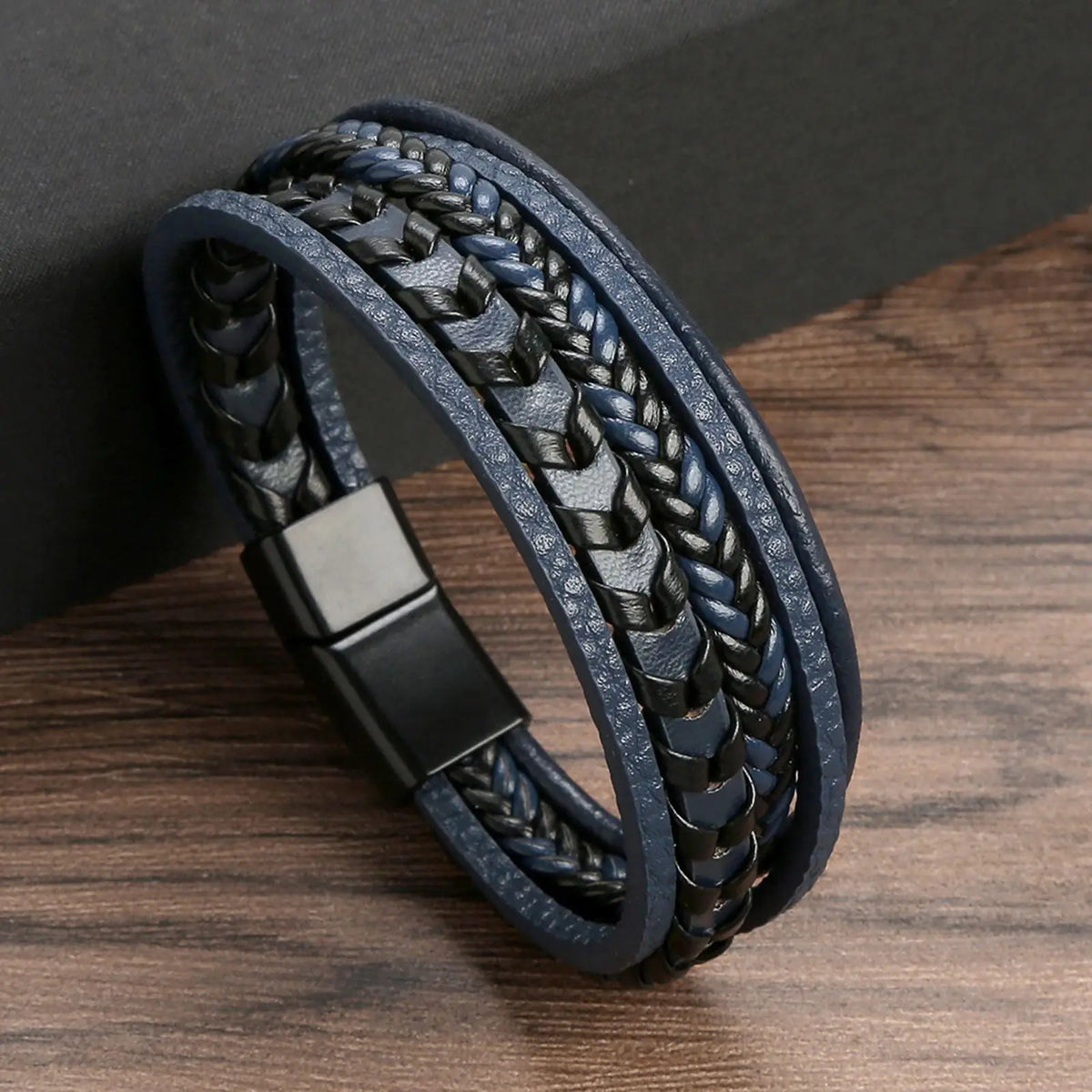 A dark blue and black multi-layer leather bracelet featuring tiger eye beads on a wooden surface.
