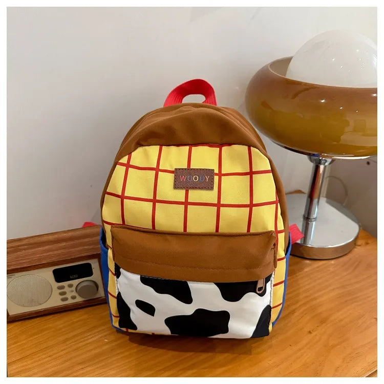 A brown and yellow plaid backpack with a cow print patch on the front, resting on a wooden table.