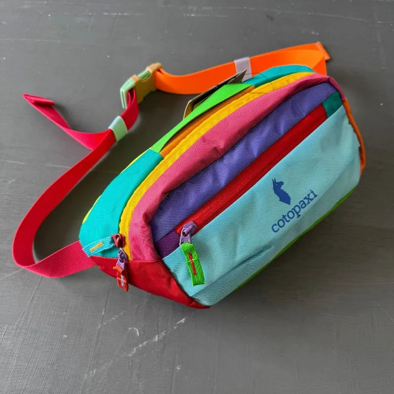Bunte, strapazierfähige Outdoor-Sport-Crossbodytasche mit mehrfarbigen Stoffpaneelen und rotem Riemen.