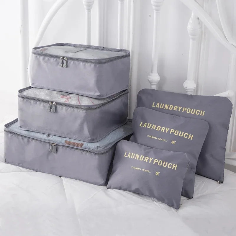 A set of three grey mesh packing cubes and matching laundry pouches are displayed on a white bed.