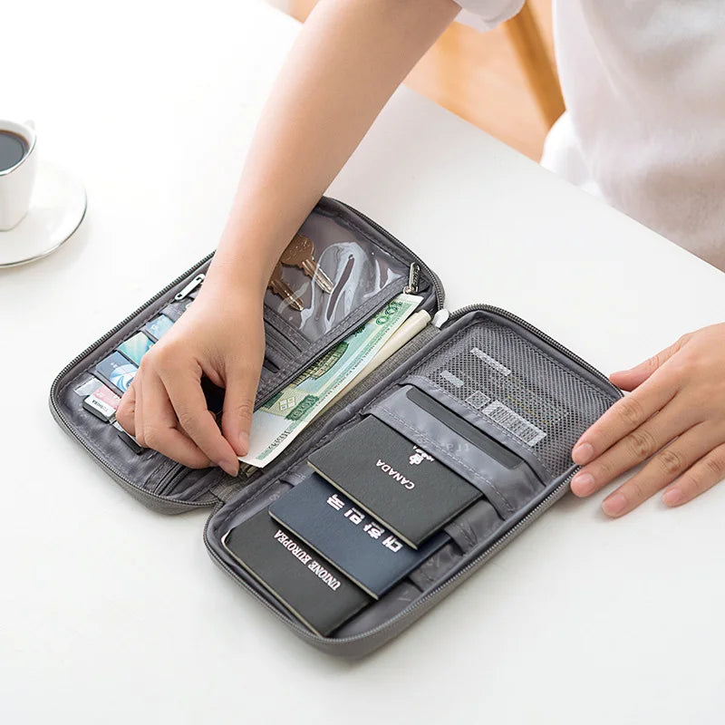 A hand is opening a dark gray multi-functional passport and document organizer showing various travel documents and cards.