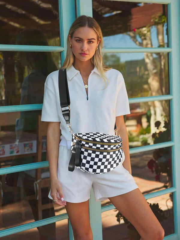 A woman wearing a white polo shirt and shorts stands in front of a glass door, holding a checkered crossbody sling bag.