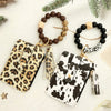A leopard print silicone leather key chain wristlet wallet with a beaded bracelet and pine greenery.