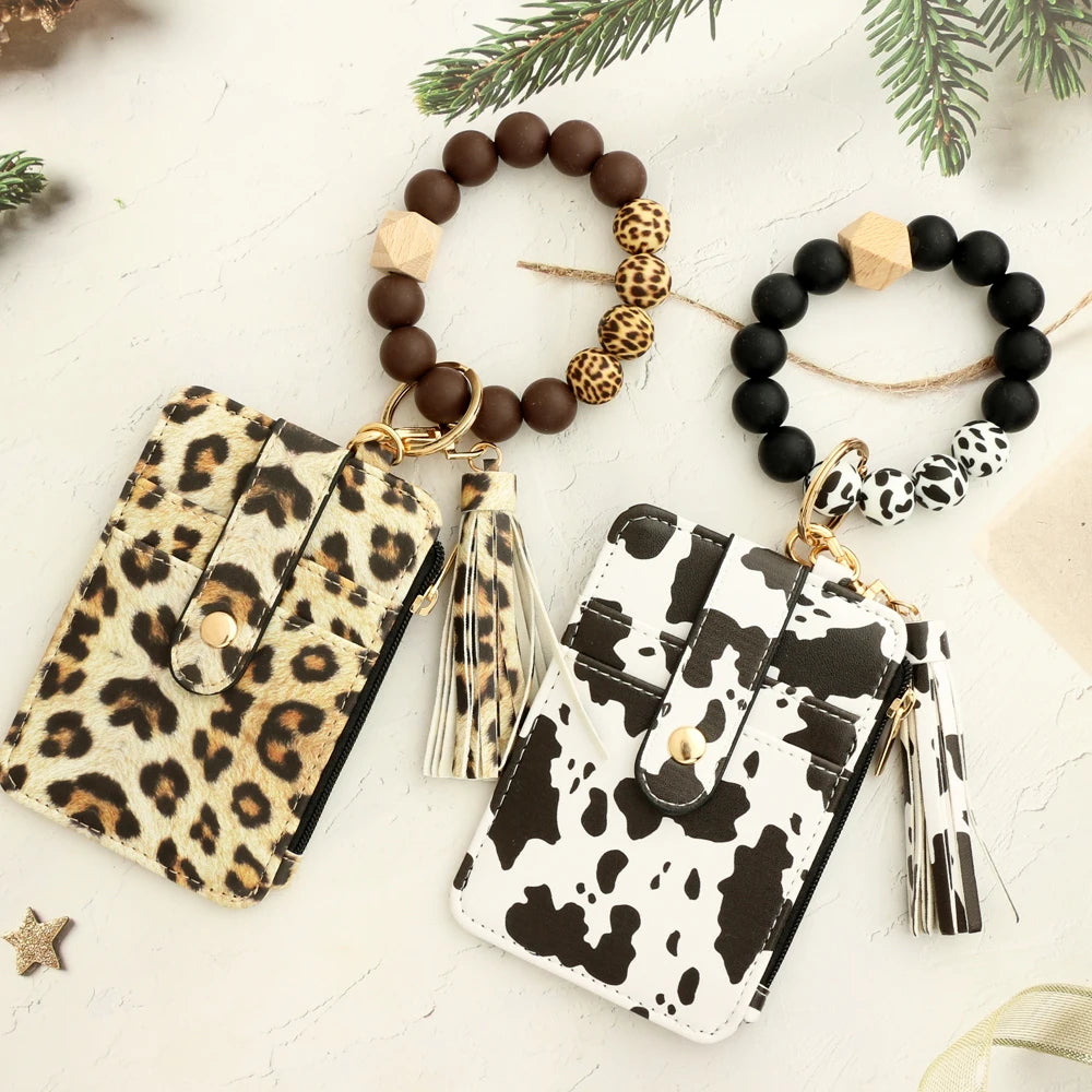 A leopard print silicone leather key chain wristlet wallet with a beaded bracelet and pine greenery.